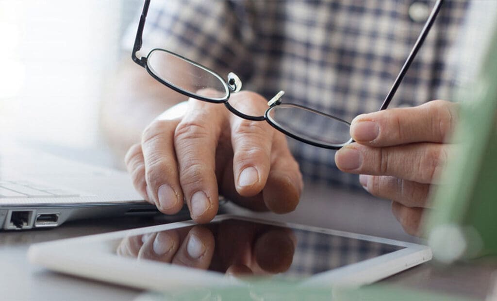 Centre for Sight - Simage of someone holding their glasses while trying to type on their tablet