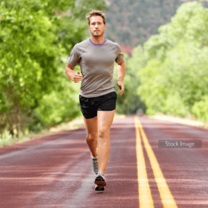 Young man running along road on a sunny day wearing shorts and a top