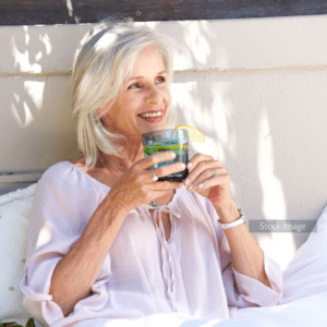 Older woman smiling and sitting outside drinking iced lemon water smiling