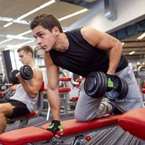 Man at the gym working out with weights on a bench dark hair and tracksuit