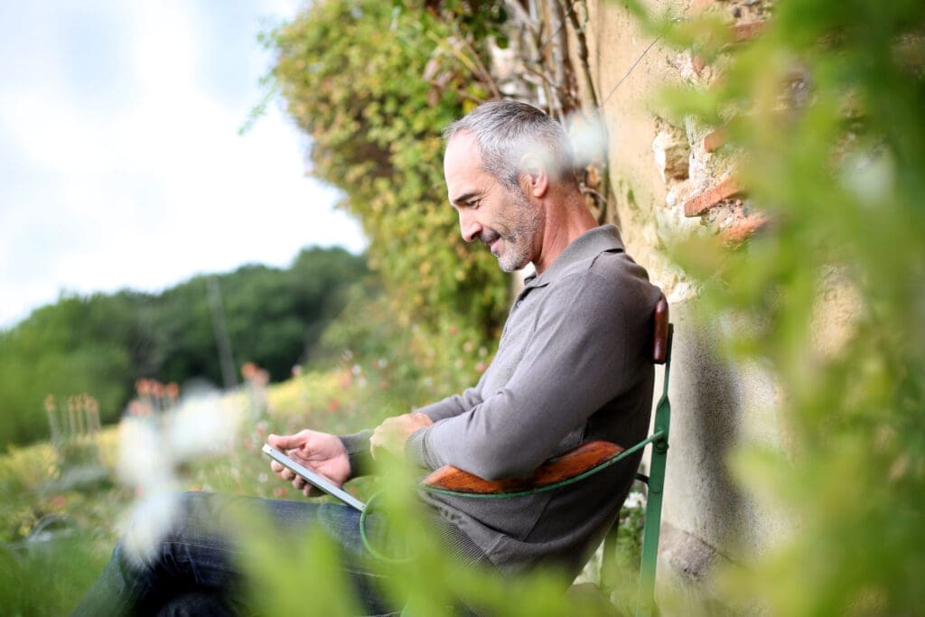 Centre for Sight - man outside sitting in the garden reading his tablet