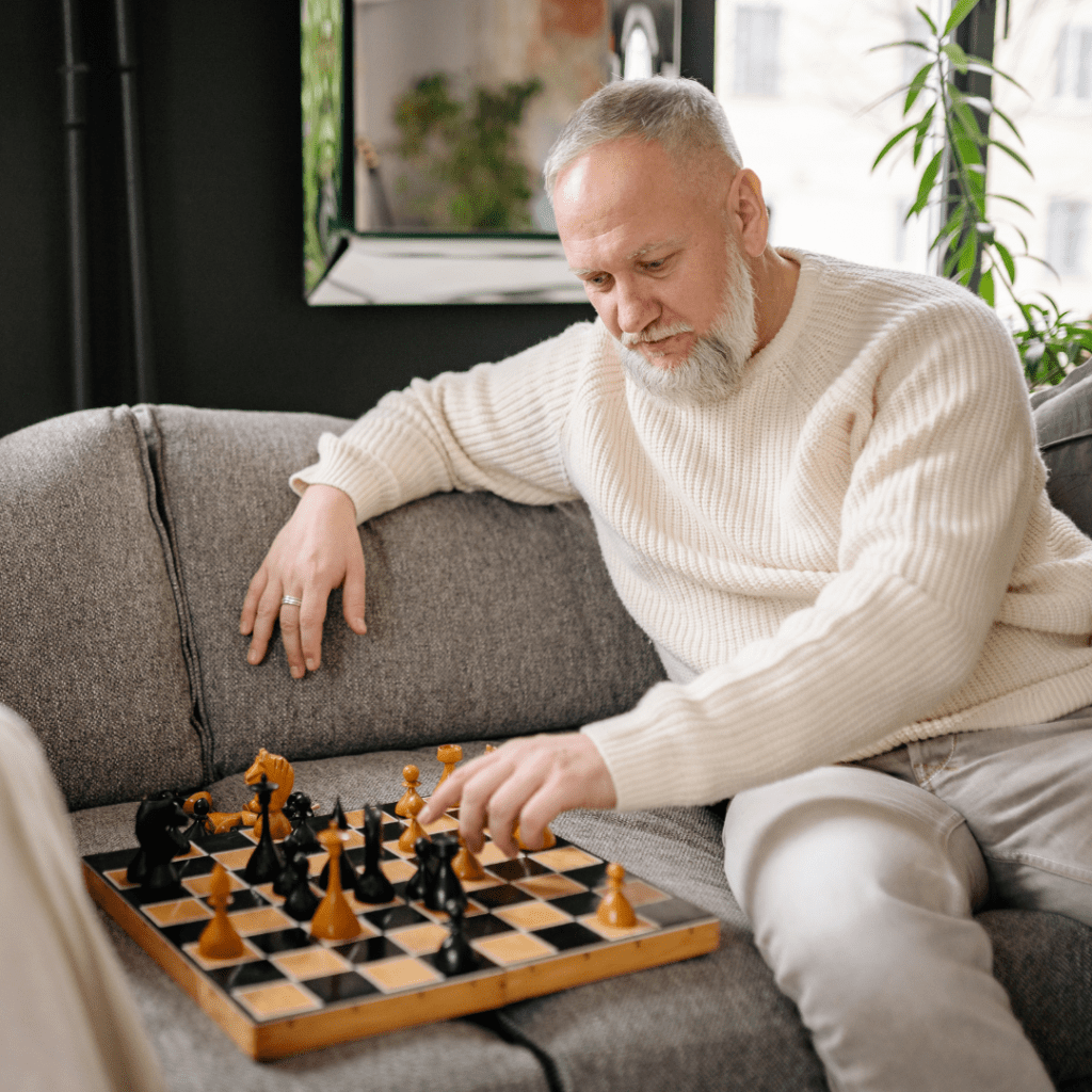 Older man with grey hair and beard playing chess by himself