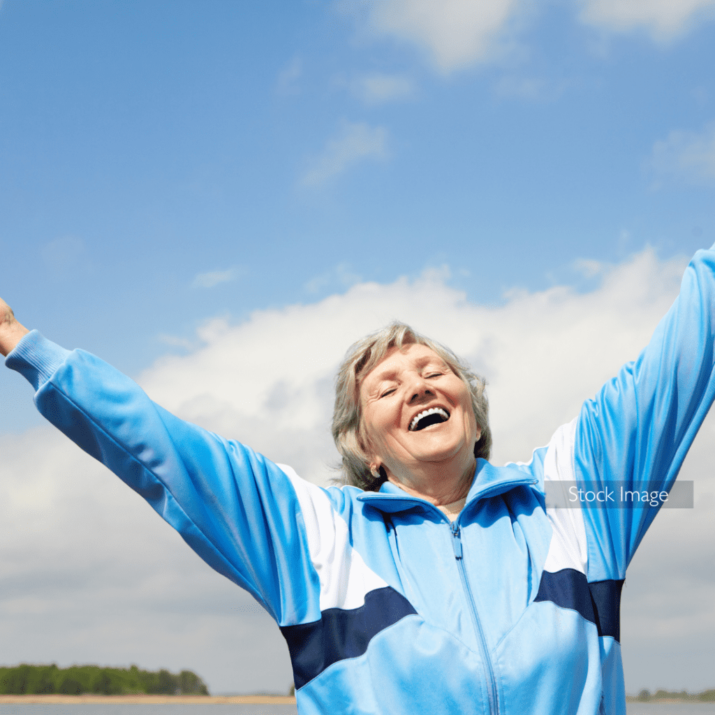 Happy older lady in field with arms in the air