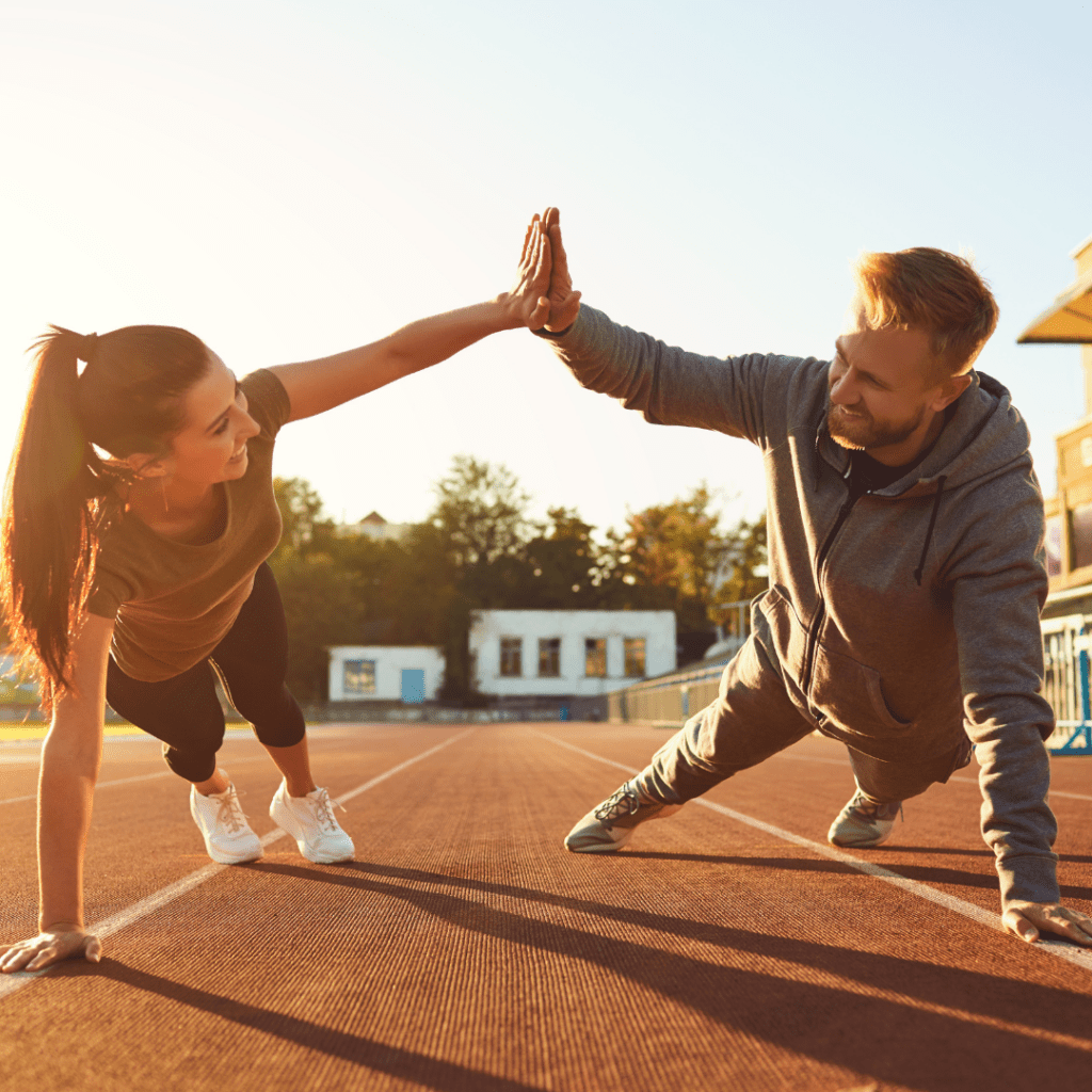 Man and woman on running track doing press up star exercises smiling in sports gear